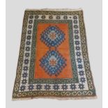 A Turkish woollen rug with two medallions upon a terracotta, blue and cream ground within multiple