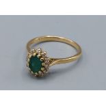 An 18ct gold Emerald and diamond cluster ring set with a central oval Emerald surrounded by