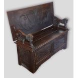 A Victorian carved oak monks bench, the carved hinged top with lion end supports, the hinged seat
