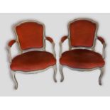 A pair of French painted open armchairs each with an upholstered back and seat with scroll arms