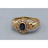 An 18ct gold ring set with a central oval sapphire surrounded by diamonds, 3.6gms, ring size J