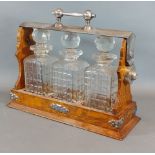 An early 20th Century oak and silver plated Tantalus with three cut glass decanters with stoppers