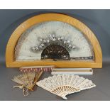 A silk fan with lacquered sticks and guards decorated with flowers within a wooden display case,
