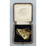 An 18ct gold brooch of shaped form set with four cabachon green stones, 9.6gms