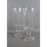 A pair of cut glass storm vases with square pedestal bases, 40cms tall