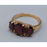 A yellow metal dress ring set with three garnets and four diamonds, 3.3gms, ring size R