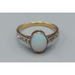 A yellow gold opal and diamond ring set with cabochon opal flanked by diamond shoulders, ring size