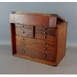 A pine table top collectors cabinet, the hinged from enclosing eight oak drawers with knob