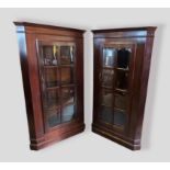 A pair of standing corner cabinets, each with a moulded cornice above an astragal glazed door raised