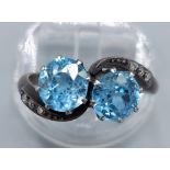 A white metal blue stone and diamond ring set with two blue stone within a crossover setting with