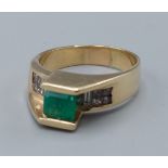 A 14ct gold ring set with a square emerald mounted above a band of diamonds 8.4gms, ring size R