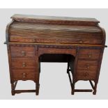 An early 20th Century oak roll top desk with seven drawers, brass drop handles and raised upon