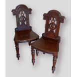 A pair of Victorian hall chairs, each with a shaped pierced back above a panel seat raised upon