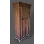 An oak hall cupboard, the moulded and carved cornice above a single panel door raised upon bun feet,