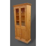 A pine bookcase, the moulded cornice above two glazed doors and two cupboard doors raised upon a