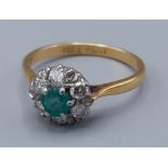 An 18ct gold and Platinum set diamond and Emerald cluster ring, with a central emerald surrounded by