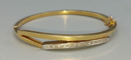 An 18ct gold bangle inset with thirteen diamonds, 6cms by 5cms, 13.4gms