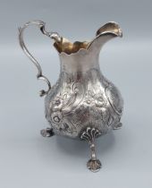 A Victorian silver cream jug with embossed decoration with shaped handle, raised upon three shaped