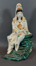 A Chinese porcelain figure in the form of Guan Yin holding a scroll upon green glazed rocky base,