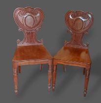 A pair of Regency mahogany hall chairs, each with a shaped back above a panel seat raised upon
