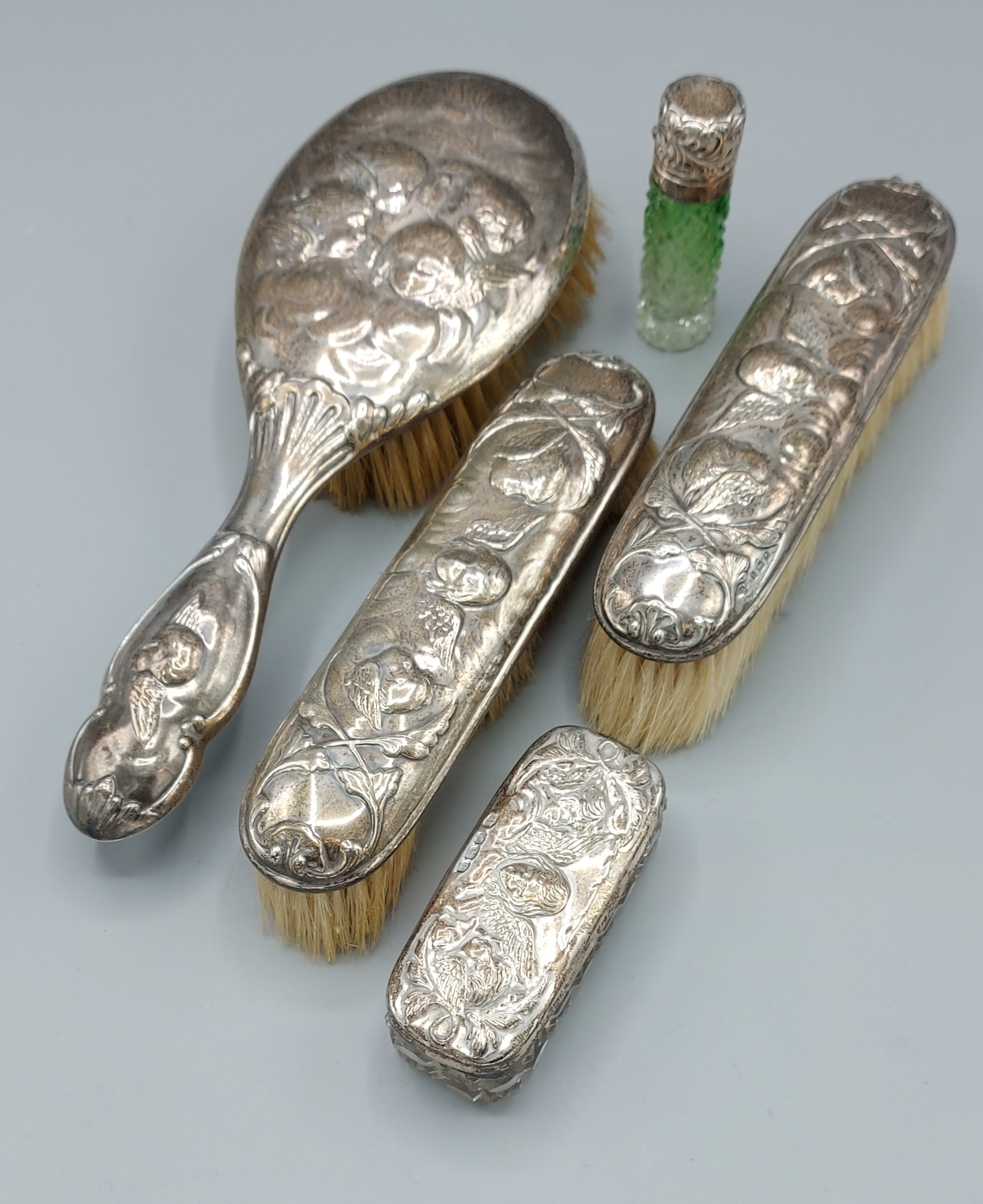 A silver backed four piece dressing table set comprising three brushes and a glass bottle, all