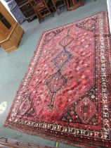 PERSIAN SHIRAZ CARPET, Three main central medallions on a red ground within multiple boarders, 252cm