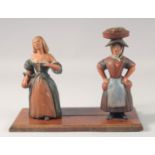 A PAINTED WOOD FOLK ART STAND with two figures. 11.5ins high.