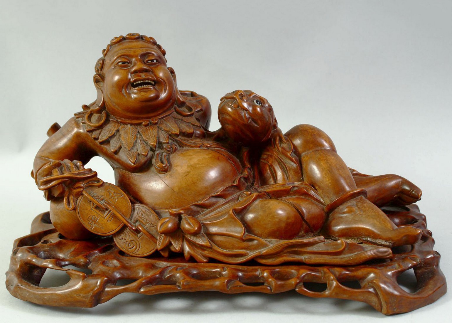 A LARGE CARVED HARDWOOD HOTEI, on a fitted carved hardwood stand, the figure reclining with a