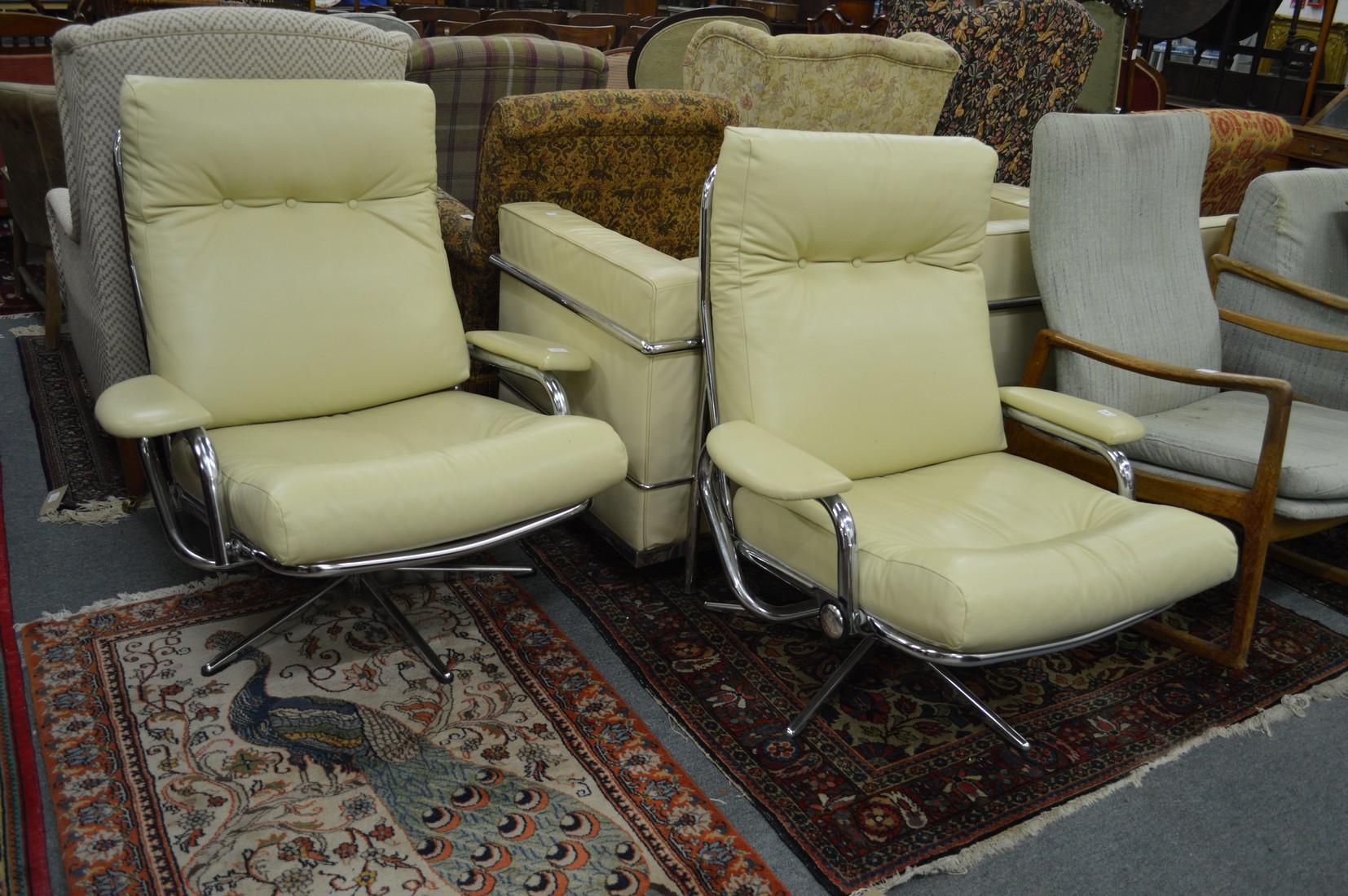 A pair of cream leather chrome framed swivel armchairs.