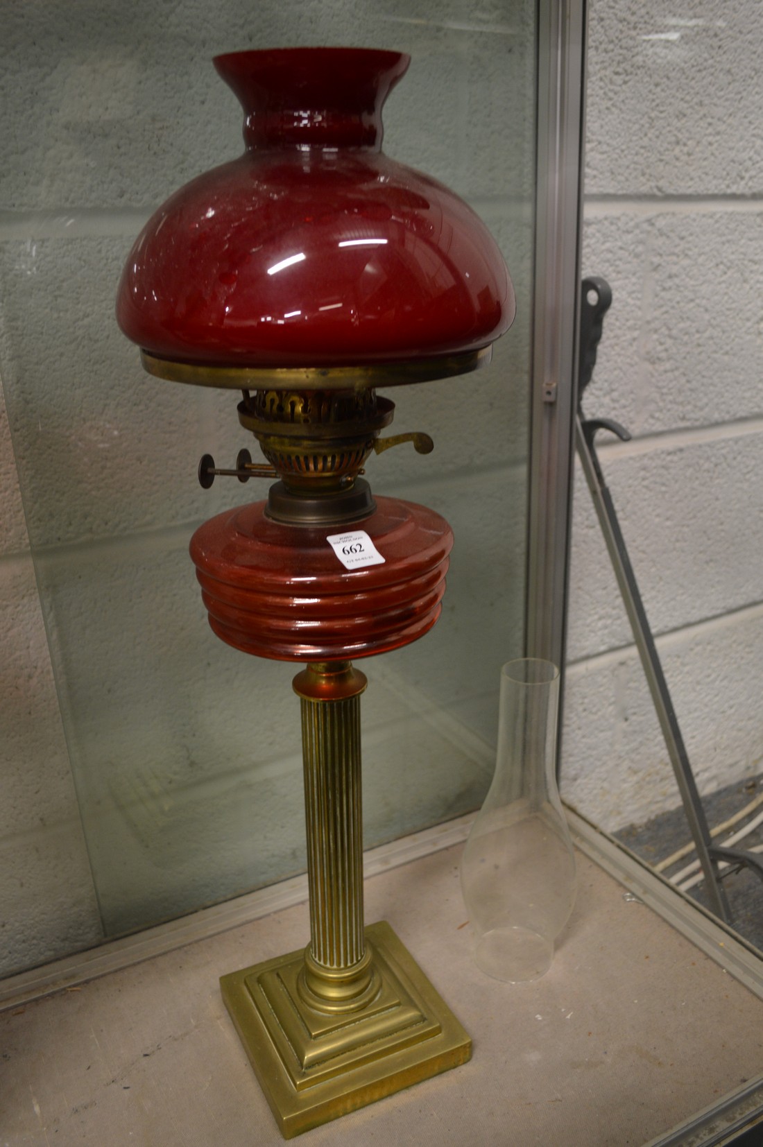 A brass and cranberry coloured glass oil lamp with a shade.