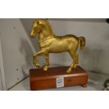 A gilded bronze model of a prancing horse on a wooden base.