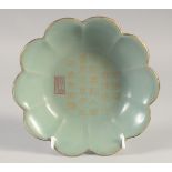 A CHINESE CELADON CALLIGRAPHIC PETAL FORM DISH, with incised inscription and gilded rim, 18cm wide.