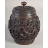 A CHINESE CARVED HARDWOOD JAR AND COVER, with relief carving depicting dragons, 15.5cm high.