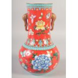 A CHINESE RED GROUND TWIN HANDLE VASE, painted with flora and butterflies, the handles molded as