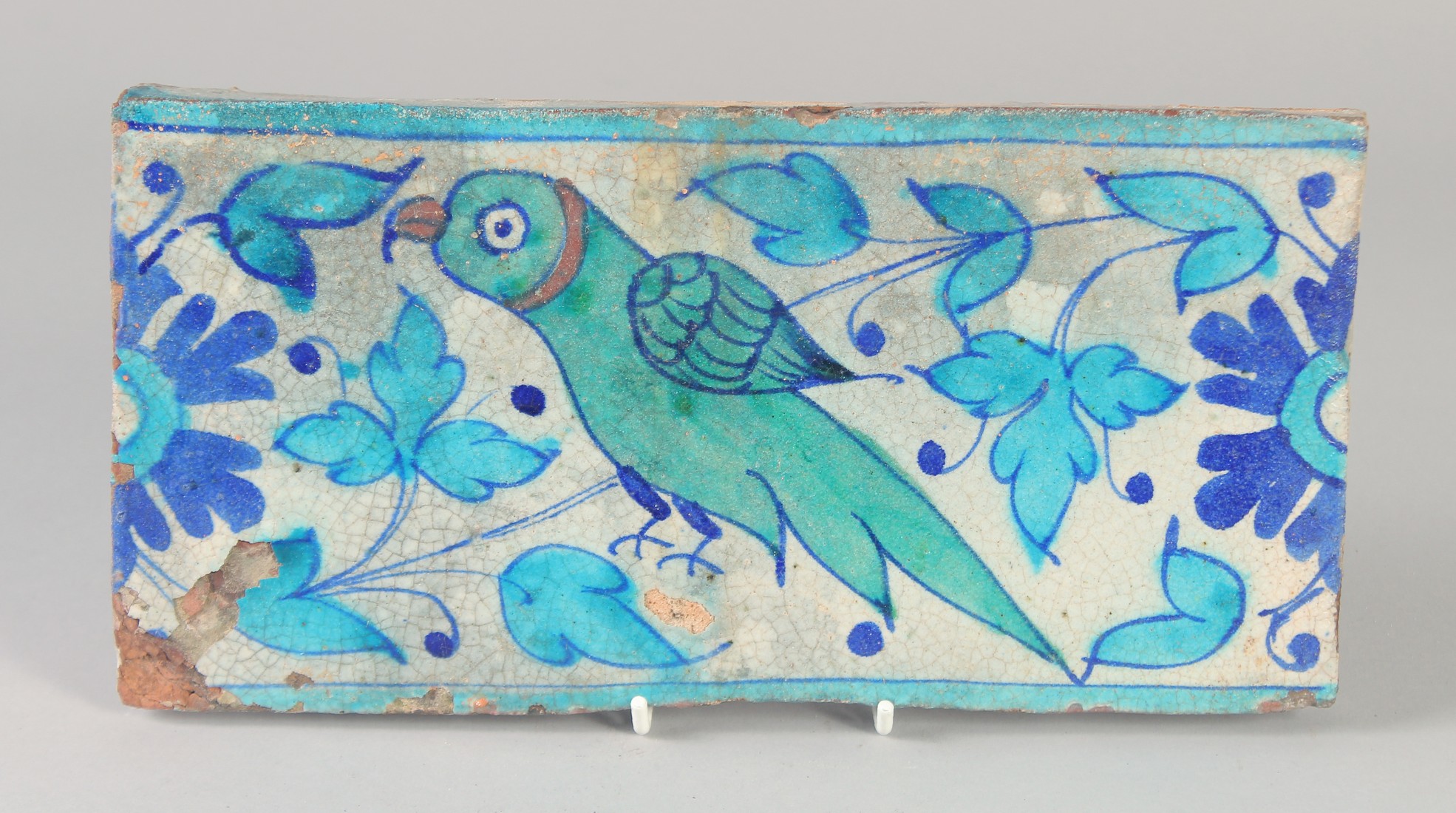 A FINE EARLY 19TH CENTURY MUGHAL INDIAN MULTAN TILE, painted with a green parrot, 28.5cm x 14.5cm.