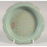A CHINESE CELADON CALLIGRAPHIC DISH, with incised inscription and gilded petal form rim, 19cm wide.