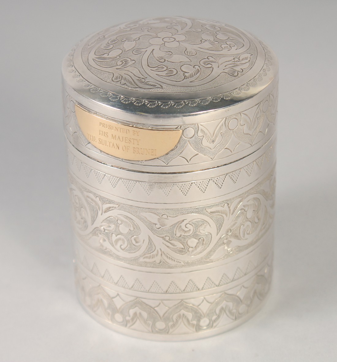 A FINELY ENGRAVED MALAY SILVER CYLINDER BOX; gifted by the sultan of Brunei, with gold plaque,