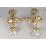 A GOOD PAIR OF GILT BRONZE CUPID WALL LIGHTS with cut glass prism drop. 12ins long.