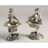 A PAIR OF SILVER PLATED YOUNG BOY AND GIRL SALTS both carrying baskets. 5.5ins high.