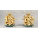 A VERY GOOD PAIR OF GILT BRONZE COMPORTS with gilt bowls and cupid supports.