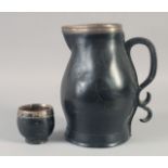 A BLACK LEATHER JUG with silver mounts and scroll handle, 14.5ins high, plus an associated silver