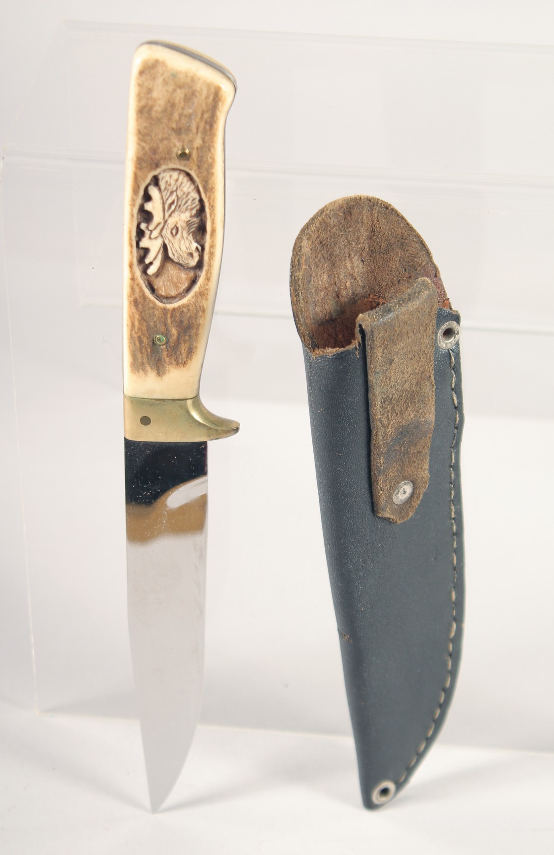 A KNIFE, with antler handle carved with a moose head, 9" long, in a leather sheath.