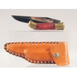 A LAGUIOLE FOLDING KNIFE, with brass and wooden handle, 7" long, in a leather sheath.