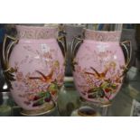 A pair of large decorative twin handled vases, pink ground painted with birds and flowers.