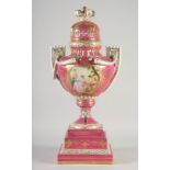 A SEVRES TWO HANDLED PORCELAIN URN AND COVER on a stand with rose pompadour ground edged in gilt.
