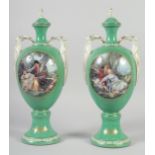 A PAIR OF CONTINENTAL GREEN GROUND TWO HANDLED URN SHAPED VASES AND COVERS. 14ins high.