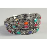 A SILVER SNAKE BRACELET set with various coloured stones.