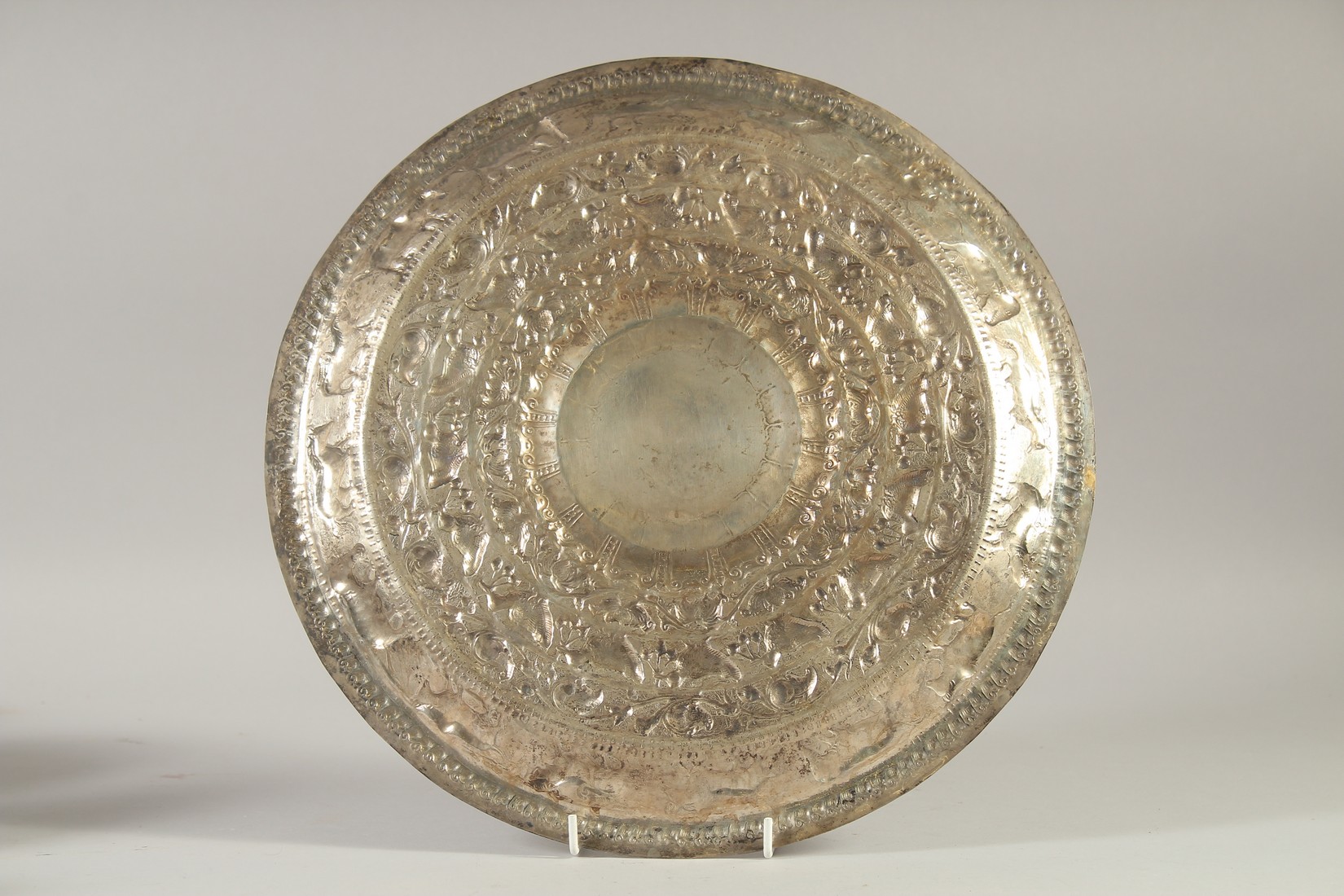 AN ISLAMIC EMBOSSED AND CHASED WHITE METAL DISH, decorated with animals, 34.5cm diameter. - Image 2 of 2