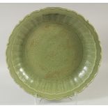 A LARGE CHINESE CELADON GLAZE CHARGER, with central carved dragon and foliate rim, 50.5cm diameter.