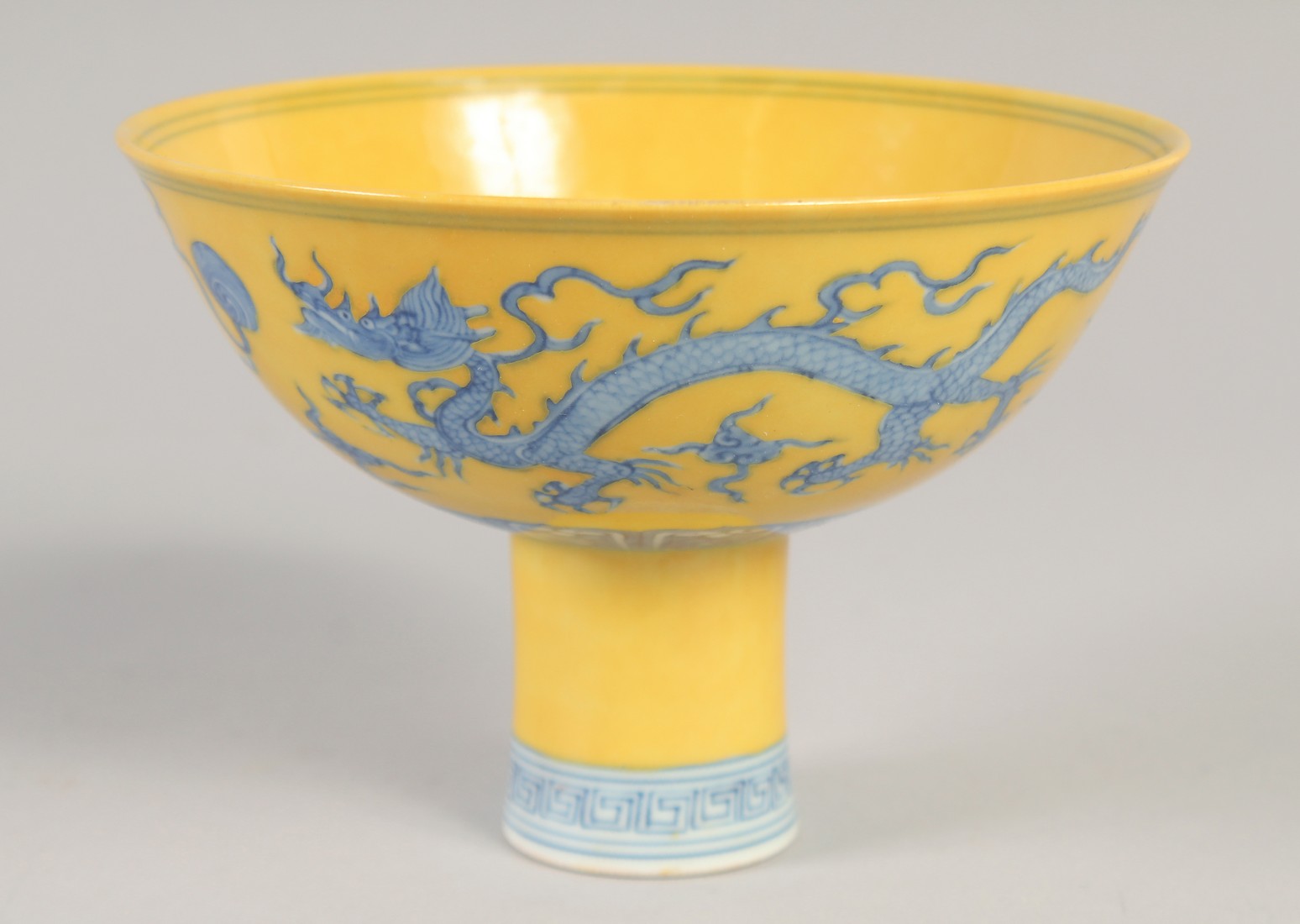 A CHINESE YELLOW GROUND BLUE AND WHITE STEM CUP, decorated with dragons, with six-character mark,